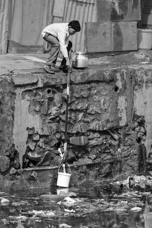 Human Right to Water in Mumbai - Meticulously filling a bucket from a leakage just above a wastewater drain